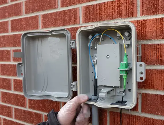 Technician opening a fiber NID on a brick wall
