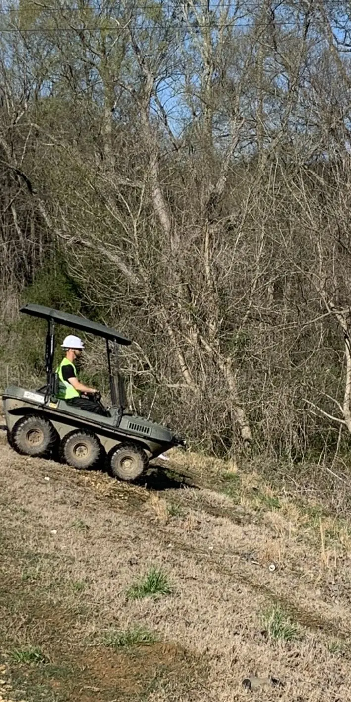 Crew member driving a tracked utility vehicle down a wooded slope